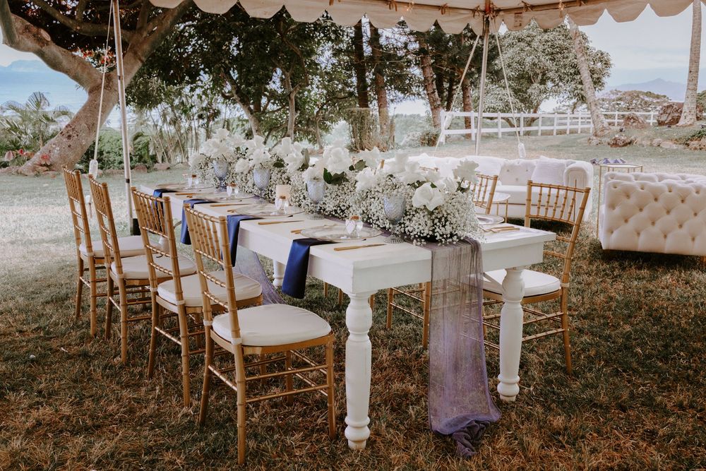 Elegant outdoor wedding reception table with purple runner and white floral centerpiece under tent.