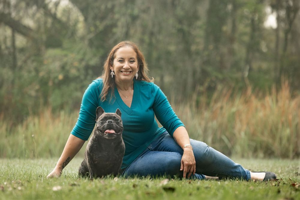 A woman sitting on a park lawn with her Frenchie resting comfortably next to her