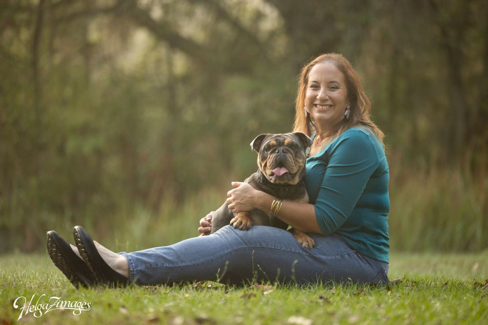 A woman sitting on a park lawn with her English Bulldog resting comfortably on her lap.