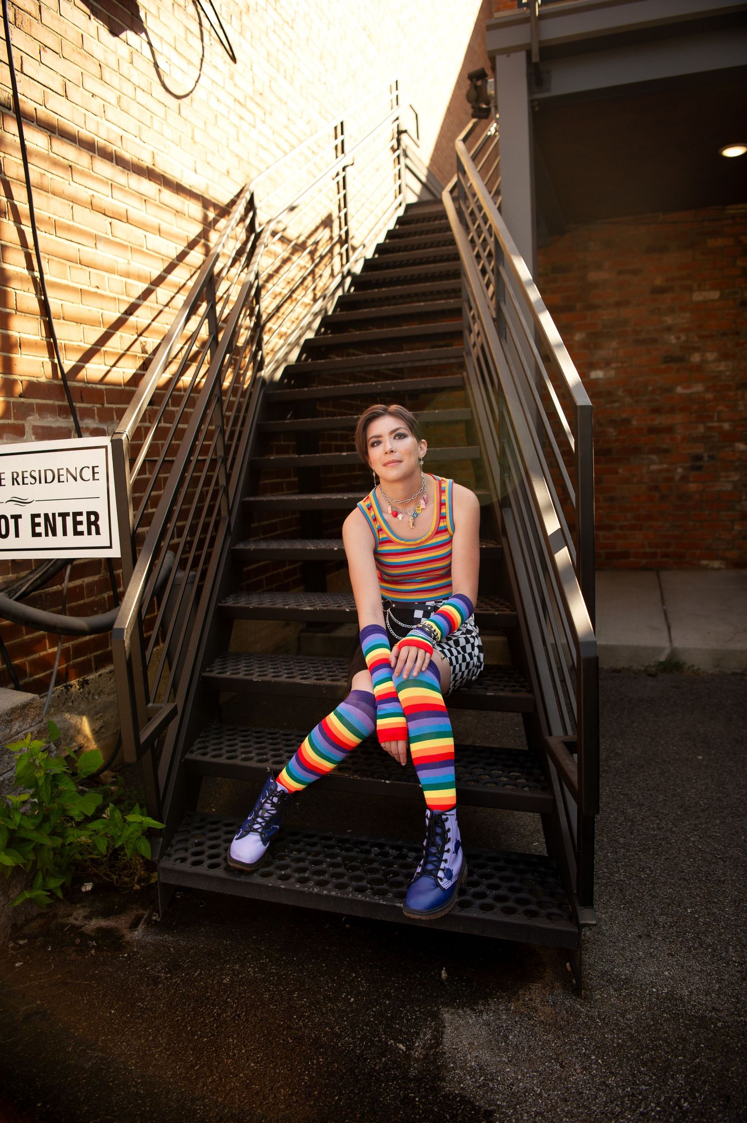 Person wearing colorful rainbow striped socks sits on outdoor metal staircase in urban setting.