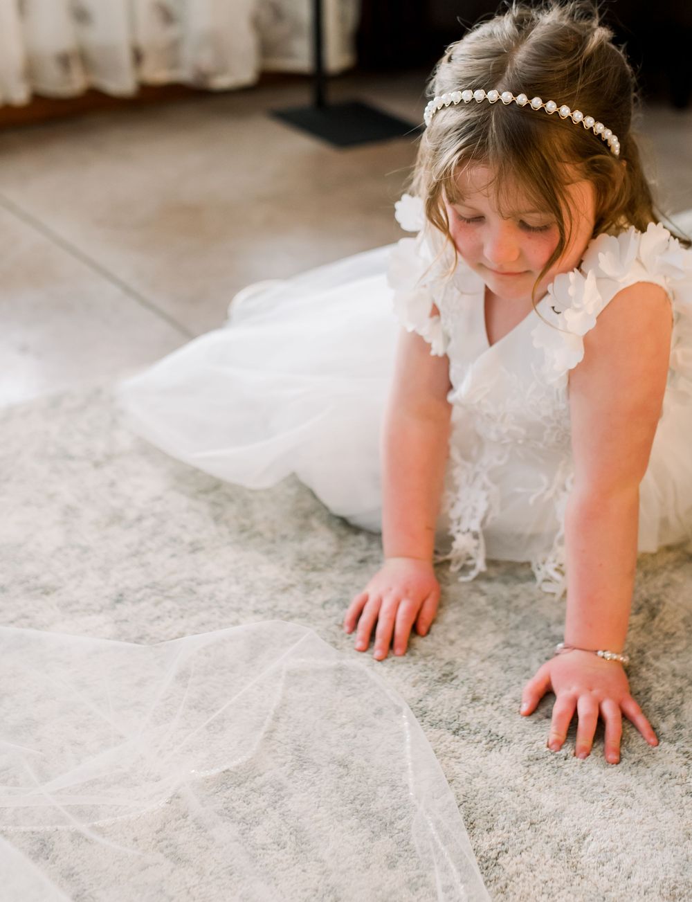 Close-up of delicate lace details on white wedding dress against light floor.