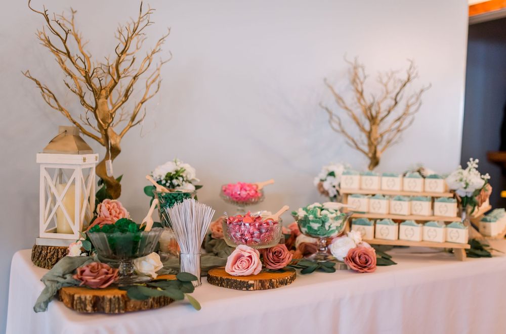 Elegant wedding reception table decor featuring rustic branches, pink roses, and white lanterns on a draped tablecloth.