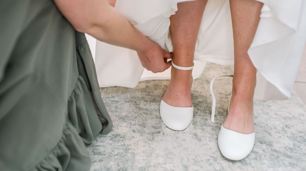 Close-up view of white bridal shoes and dress hem on a stone floor during a wedding ceremony.