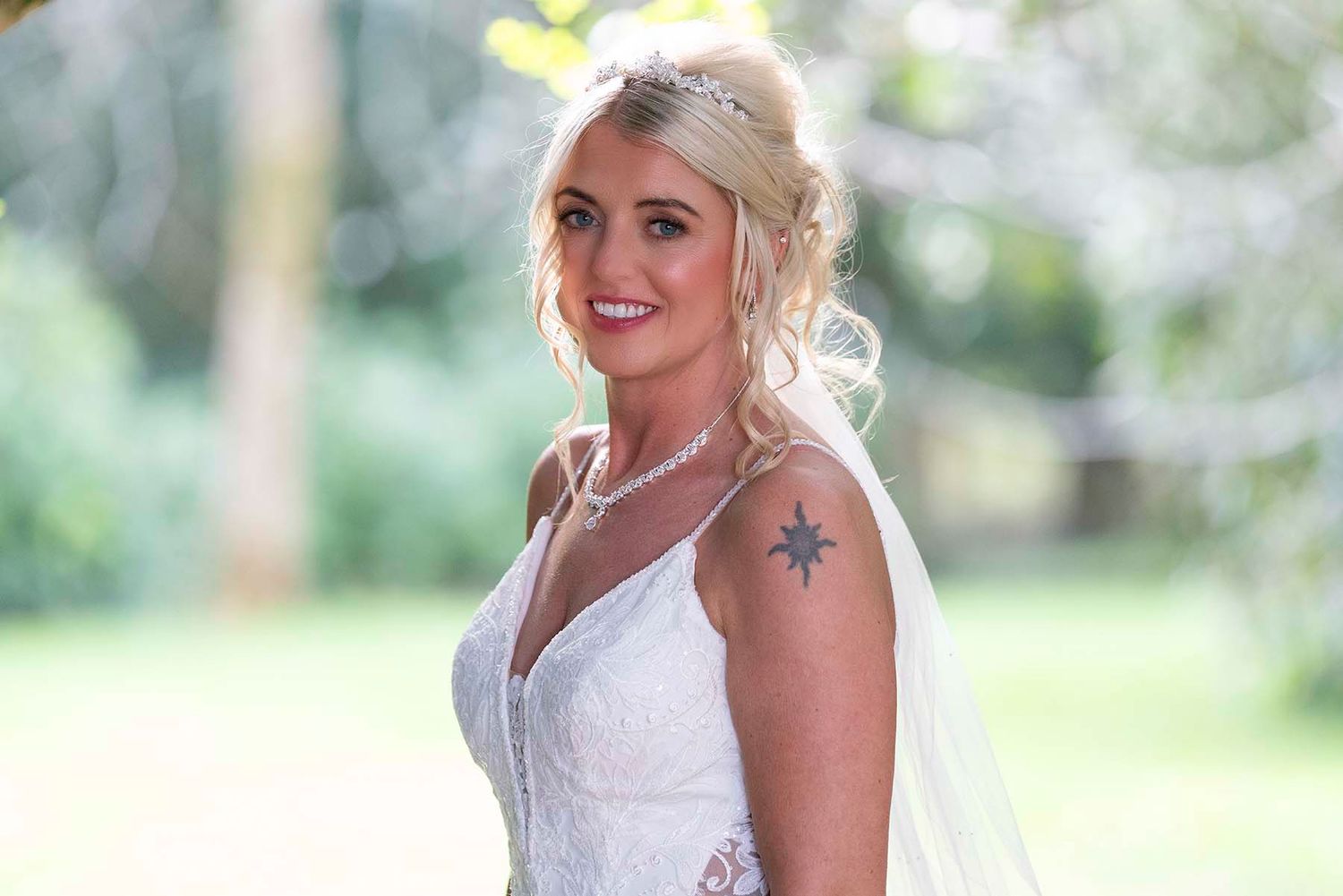 A bride in a white wedding dress poses outdoors in a natural setting with soft green foliage in the background.