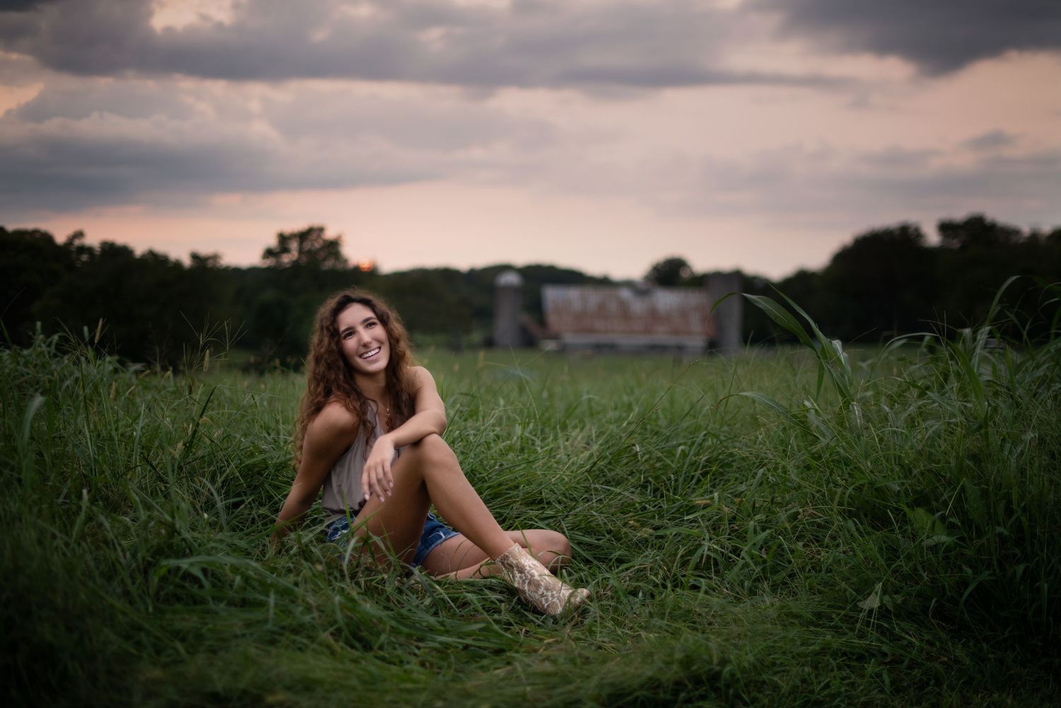 A person sits in a lush green field during sunset creating a dreamy outdoor portrait scene.