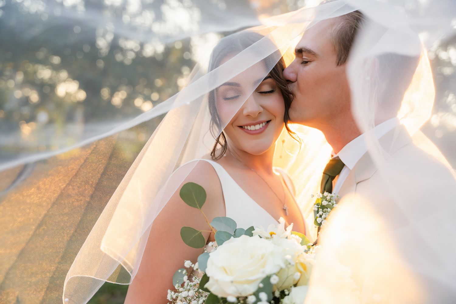 Groom kissing bride's forehead under a veil at golden hour at Twisted Oak Farm, Vero Beach, FL