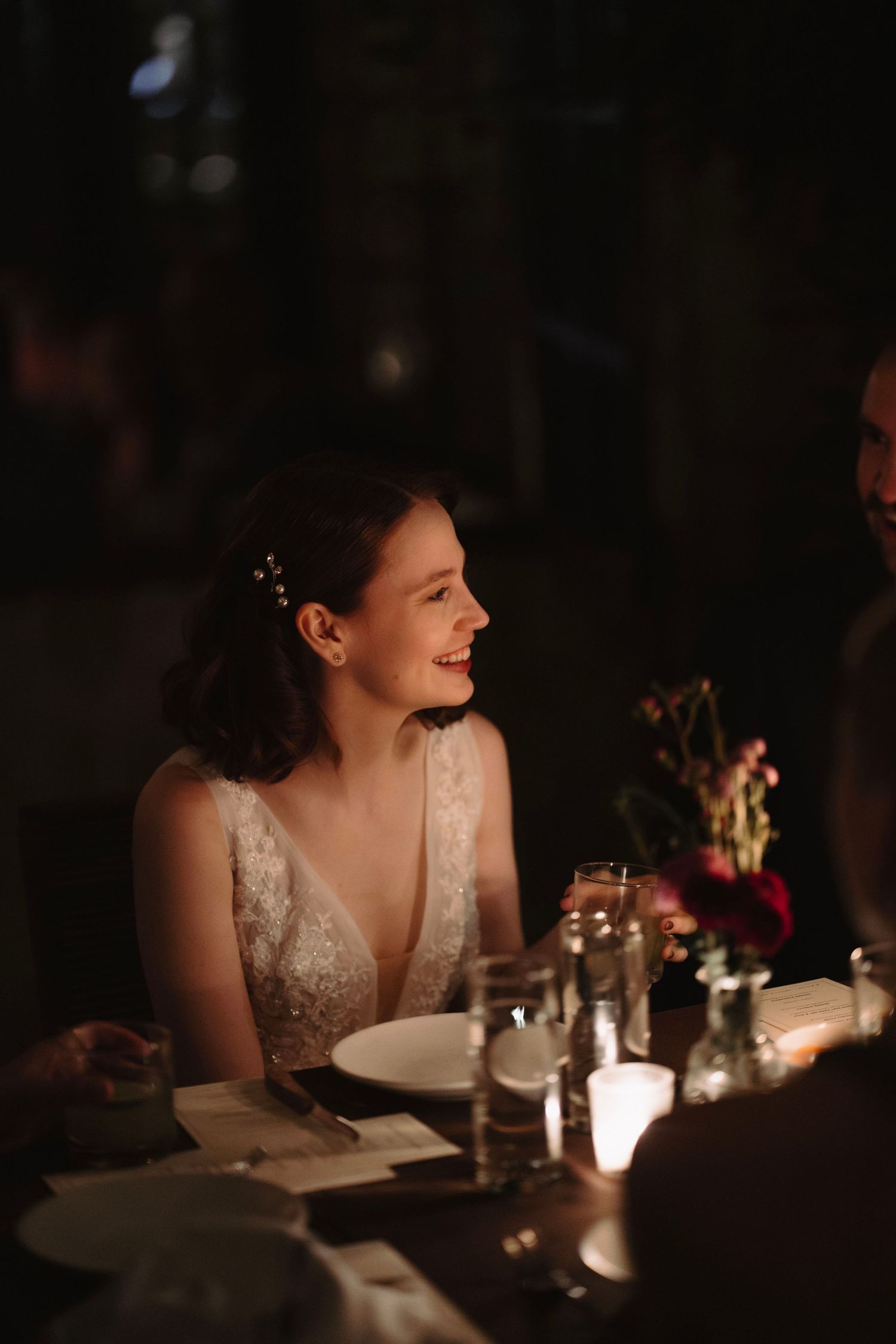 Bride and groom laughing with a guest at an outdoor evening wedding reception with warm string lights.