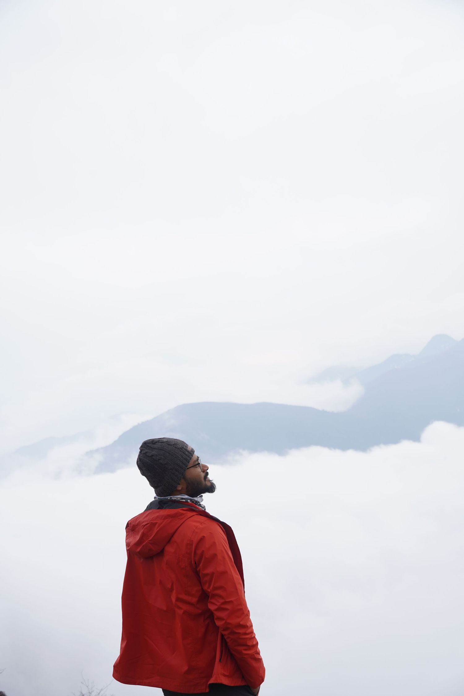 Minimalist portrait of a trekker in a red jacket standing against a vast, white mountain sky, captured by devineFLAW.