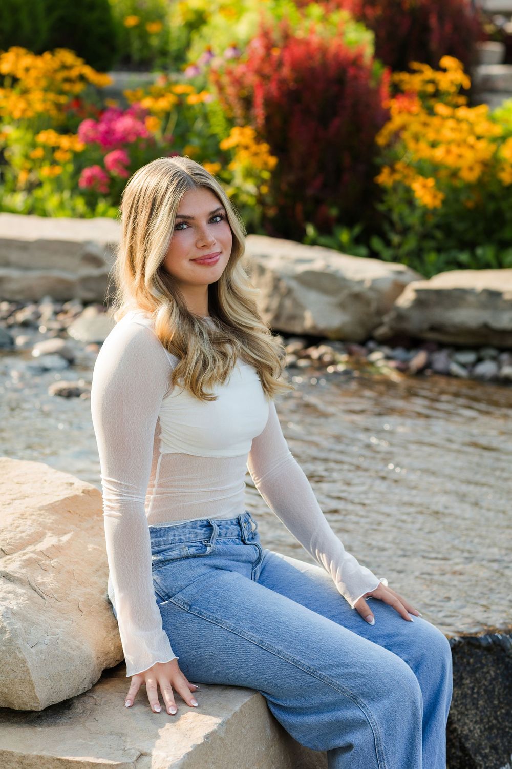 Casual portrait on stone wall with colorful garden flowers in background during golden hour.