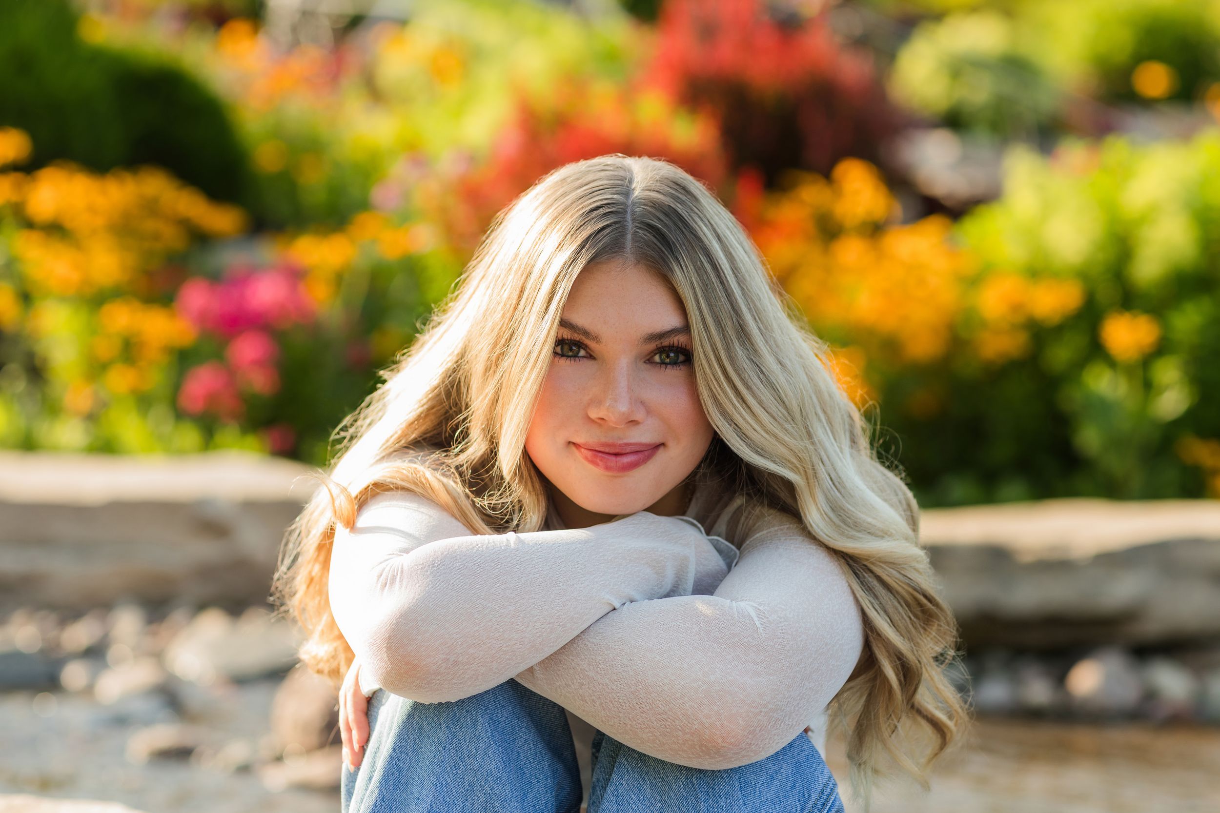 A woman poses in a garden filled with vibrant yellow and orange flowers on a sunny day.