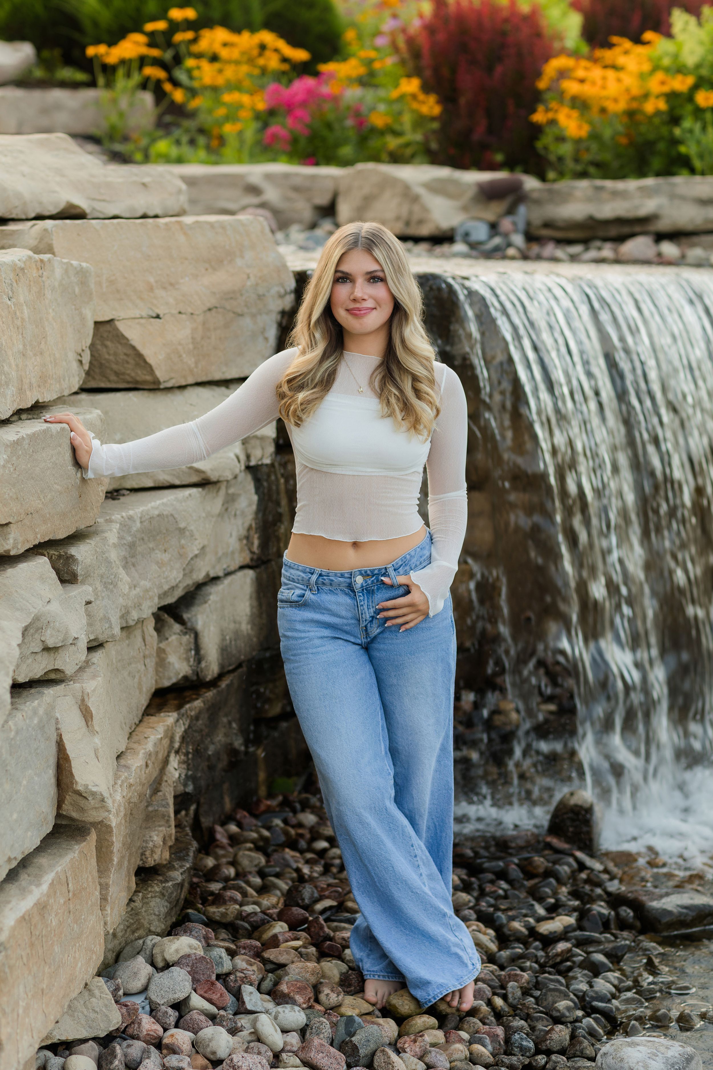 Scenic waterfall backdrop with rocks and colorful flowers creates perfect outdoor photo setting.