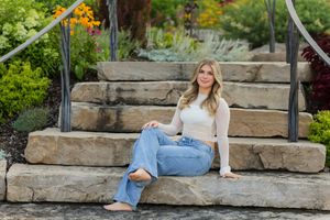 Woman in white dress sitting on stone steps in an outdoor garden setting at sunset.