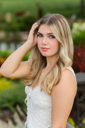 Woman in white lace dress poses outdoors in a garden setting with soft natural lighting.