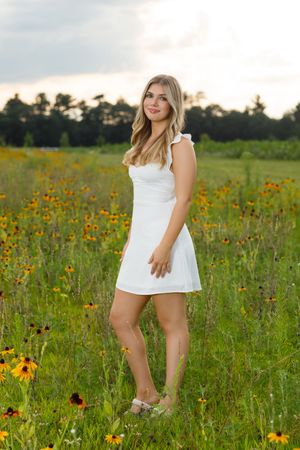 Woman in white dress poses in a wildflower field with black-eyed susans at golden hour.
