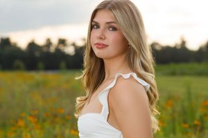 A woman in a white dress poses gracefully in a vibrant field of orange wildflowers at sunset.
