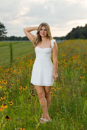 A person in a white summer dress poses gracefully in a wildflower meadow filled with black-eyed susans at sunset.