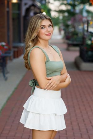 Summer fashion shoot on brick sidewalk featuring sage green top and white ruffle skirt.