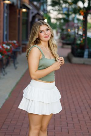 Urban fashion photoshoot on brick sidewalk featuring summer outfits in sage green and white ruffled styles.