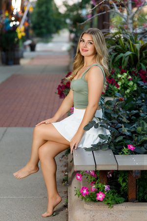 Summer fashion portrait on stone bench surrounded by pink flowers and greenery.