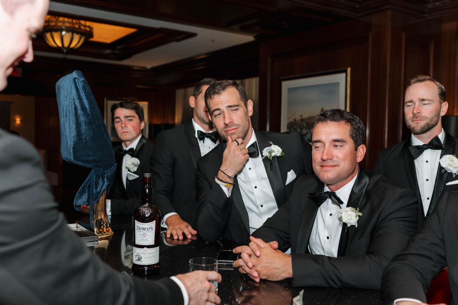 A group of formally dressed people in tuxedos gather around a table with champagne bottles and glasses.