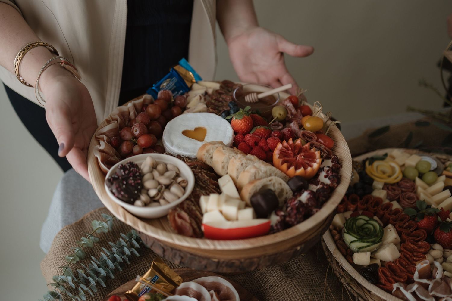 A hand reaches for food from a spread of dishes including meats and appetizers on a wooden table.