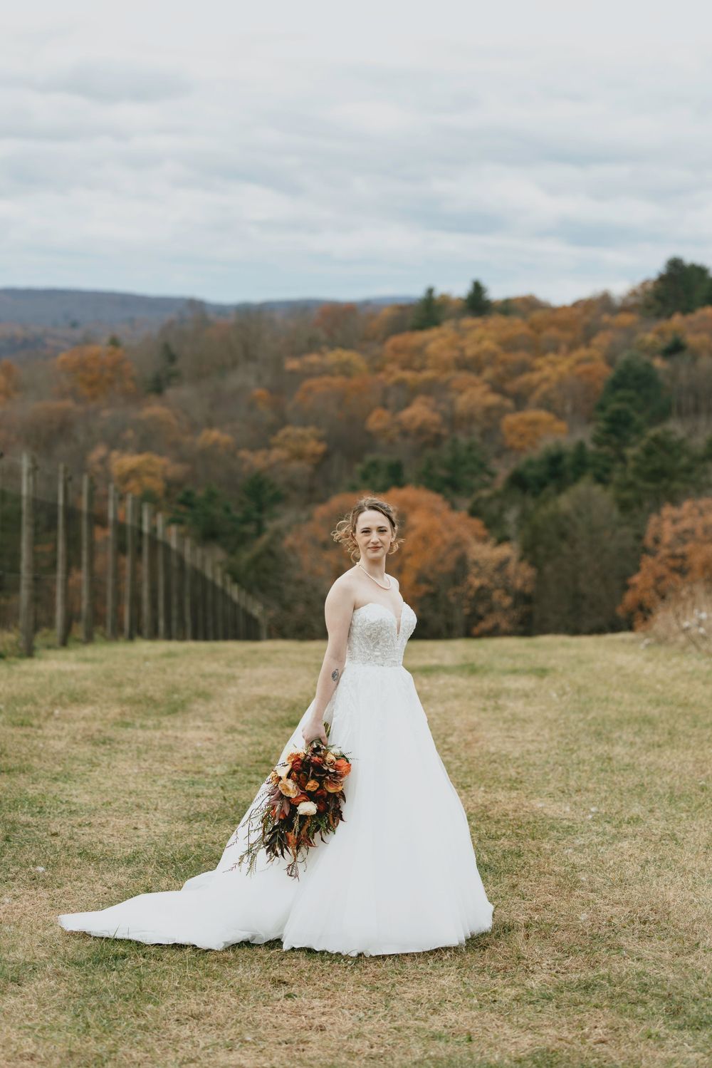 A white wedding dress stands out against an autumn hillside with golden foliage and a row of utility poles in the background.