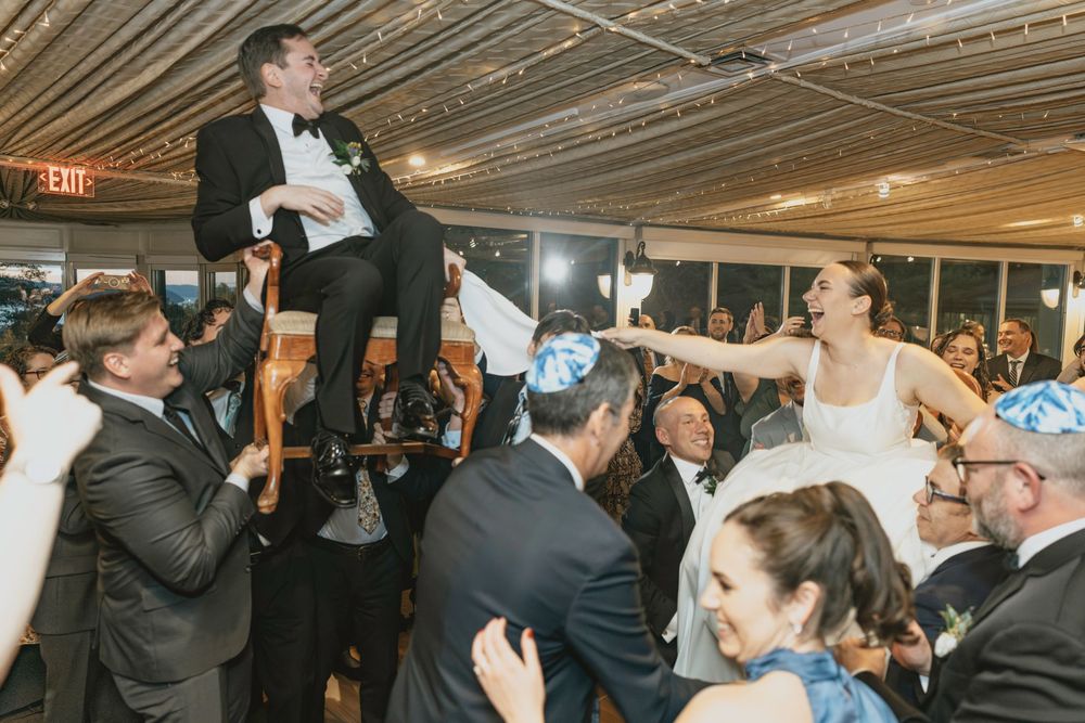 Guests and wedding party members dancing energetically at an indoor reception with decorative ceiling lights.