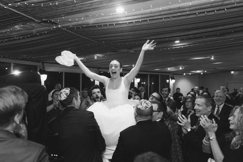 Black and white panoramic view of a wedding reception dance floor with string lights overhead.