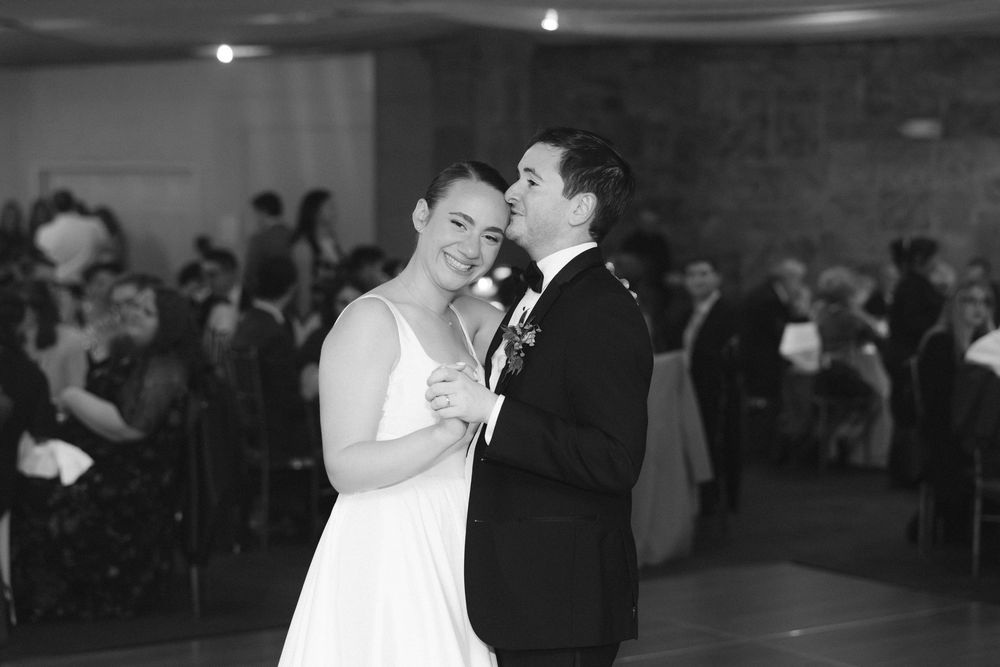 A couple shares a romantic dance moment at a wedding reception in a dimly lit ballroom.