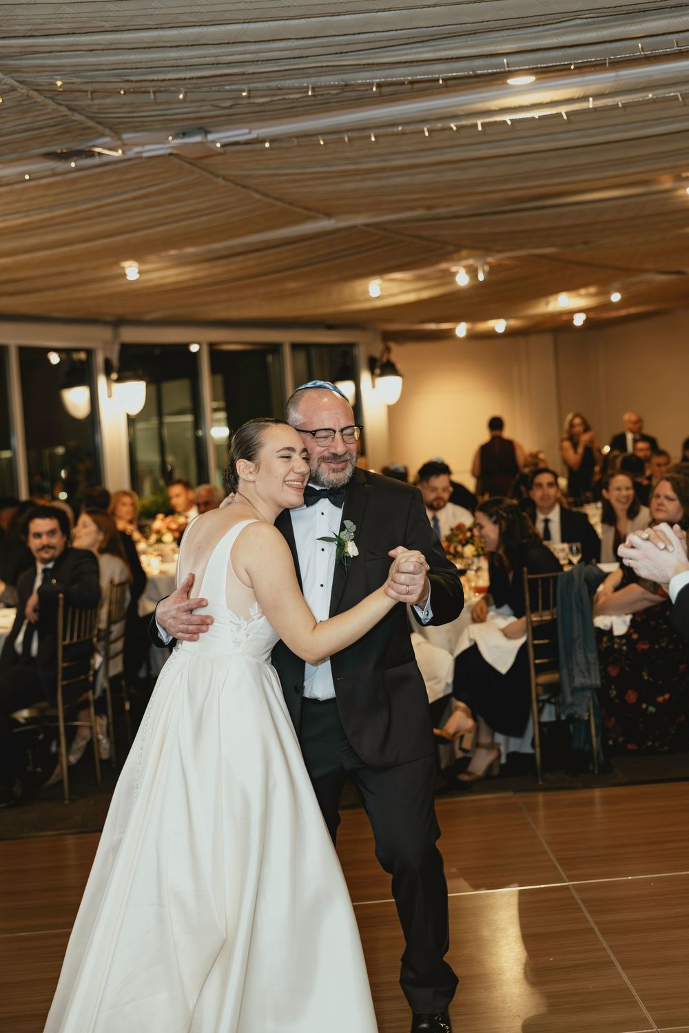 Couples dance together during a wedding reception in an elegant venue with string lights overhead.