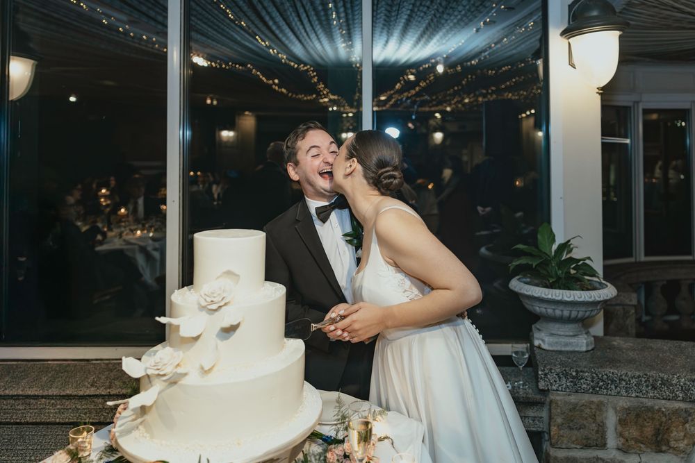 Wedding party members share bites of white wedding cake during an evening reception celebration.