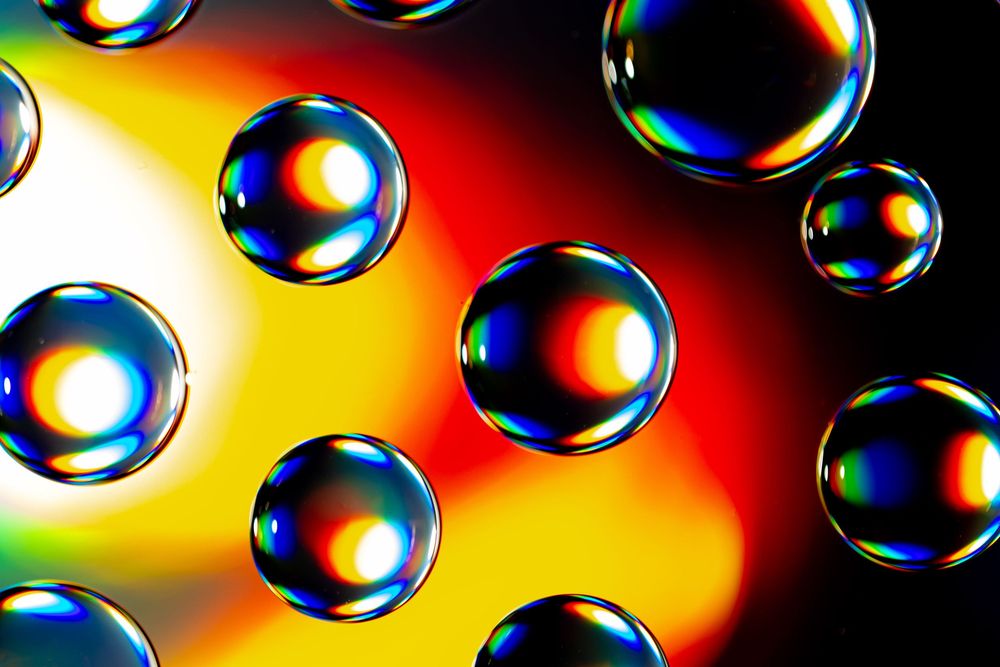 Colorful soap bubbles floating against vibrant yellow and red background with rainbow iridescent reflections.