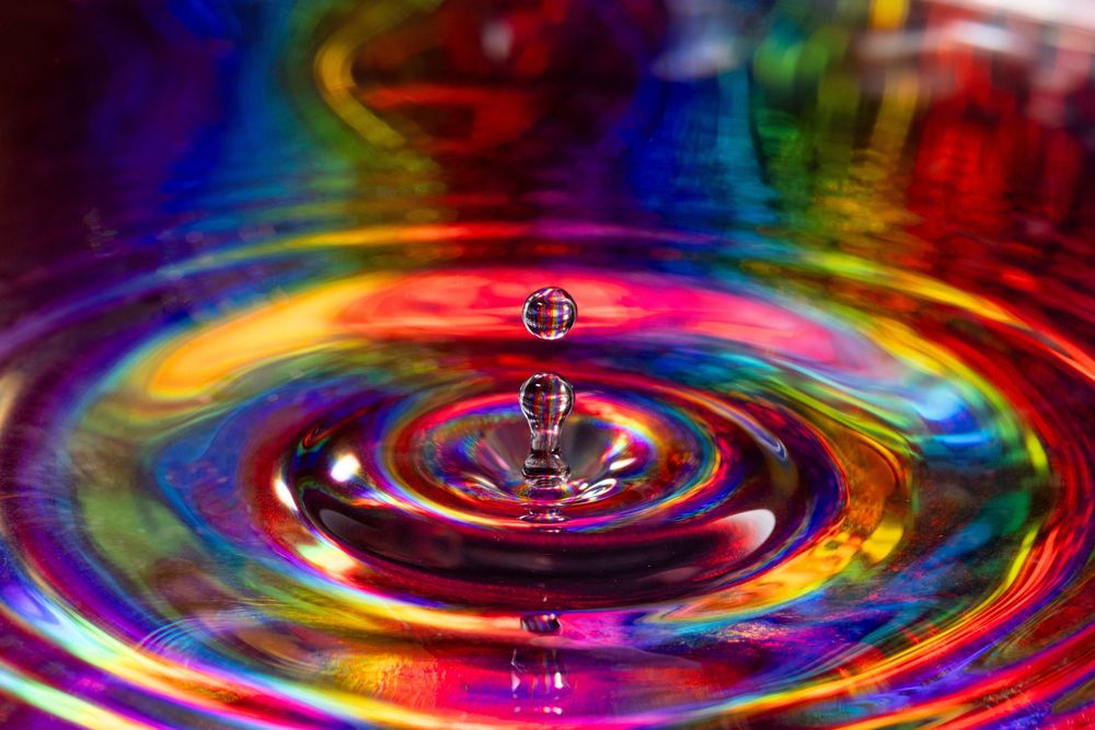 Series of rainbow-colored water ripples forming concentric circles against a dark background.