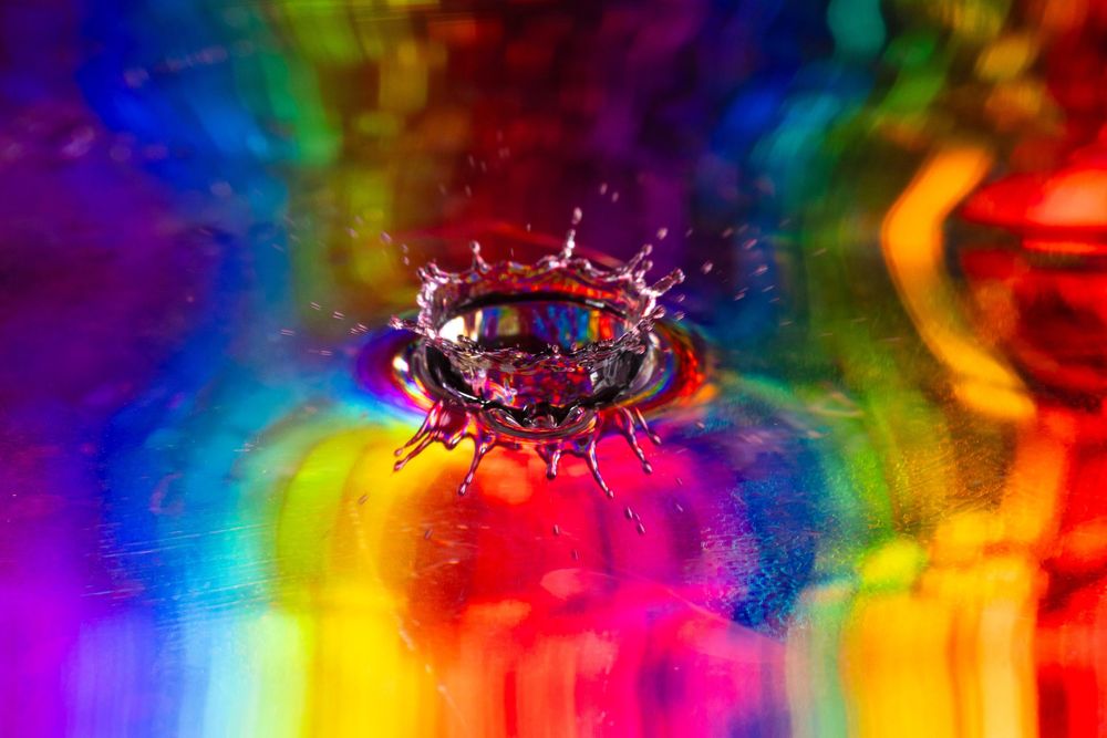High-speed photography captures colorful water droplet crown formations against vibrant rainbow background.