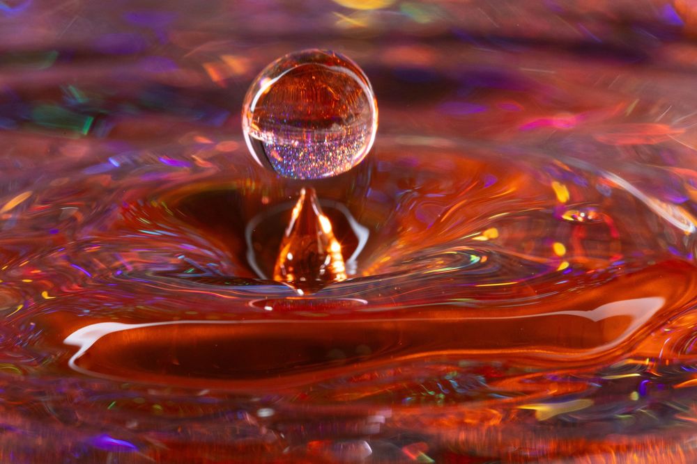Water droplets splashing and creating ripples in orange and red tinted liquid.
