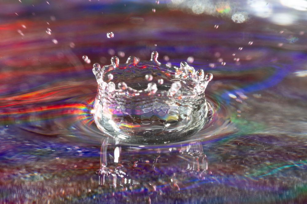 Water drops splashing and creating crown-like formations with multicolored reflections.