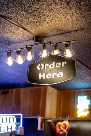 Illuminated Order Here sign hanging from ceiling with Edison bulbs above bar area.