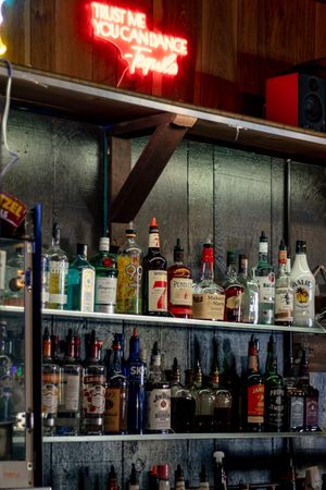 Bar shelf stocked with liquor bottles below neon Trust Me You Can Dance tequila sign at Tommy's Tavern in Yelm bar marketing photoshoot