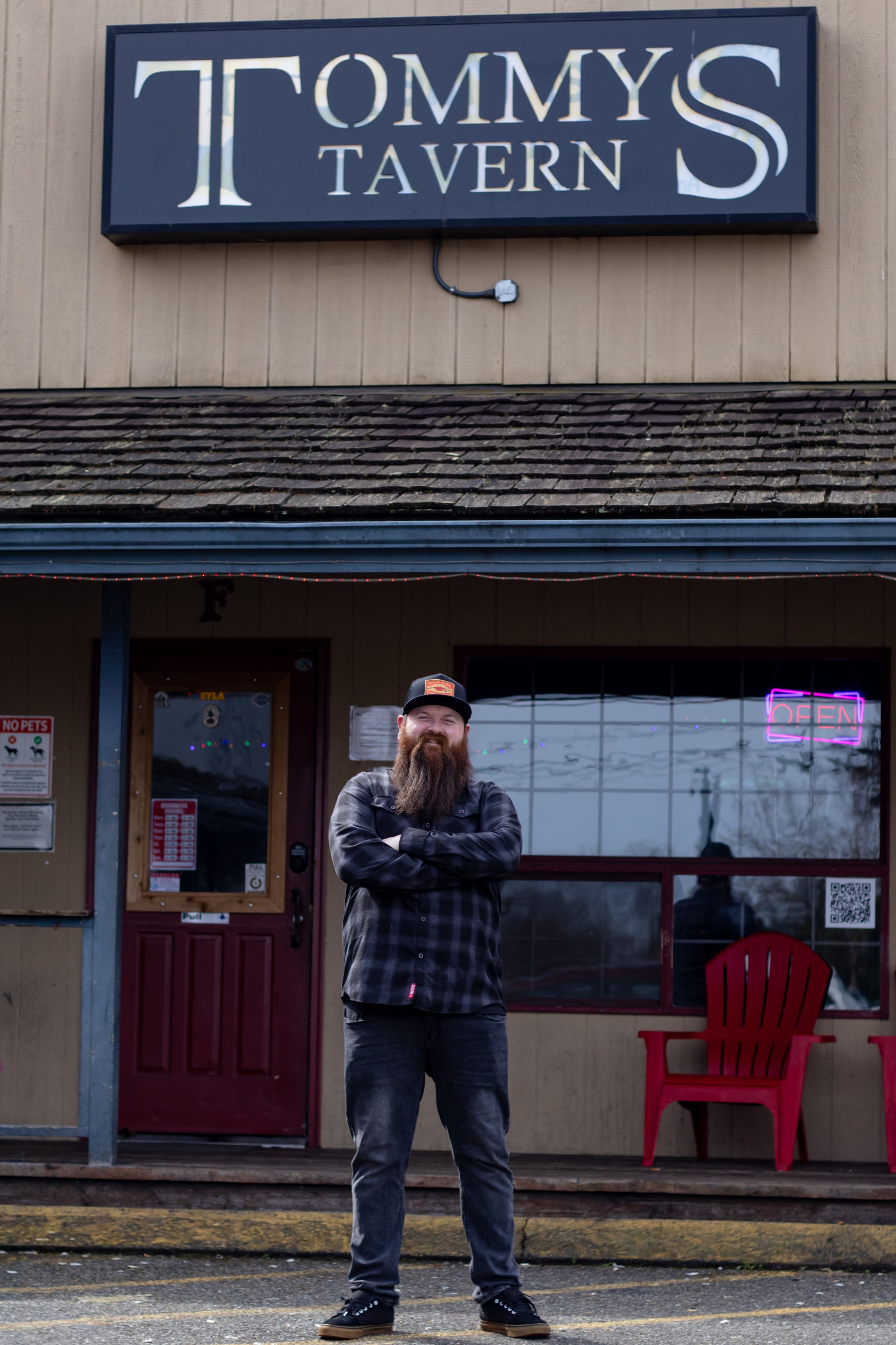 Owner standing with crossed arms standing in front of Tommy's Tavern exterior sign during marketing photo session with Yelm WA photographer