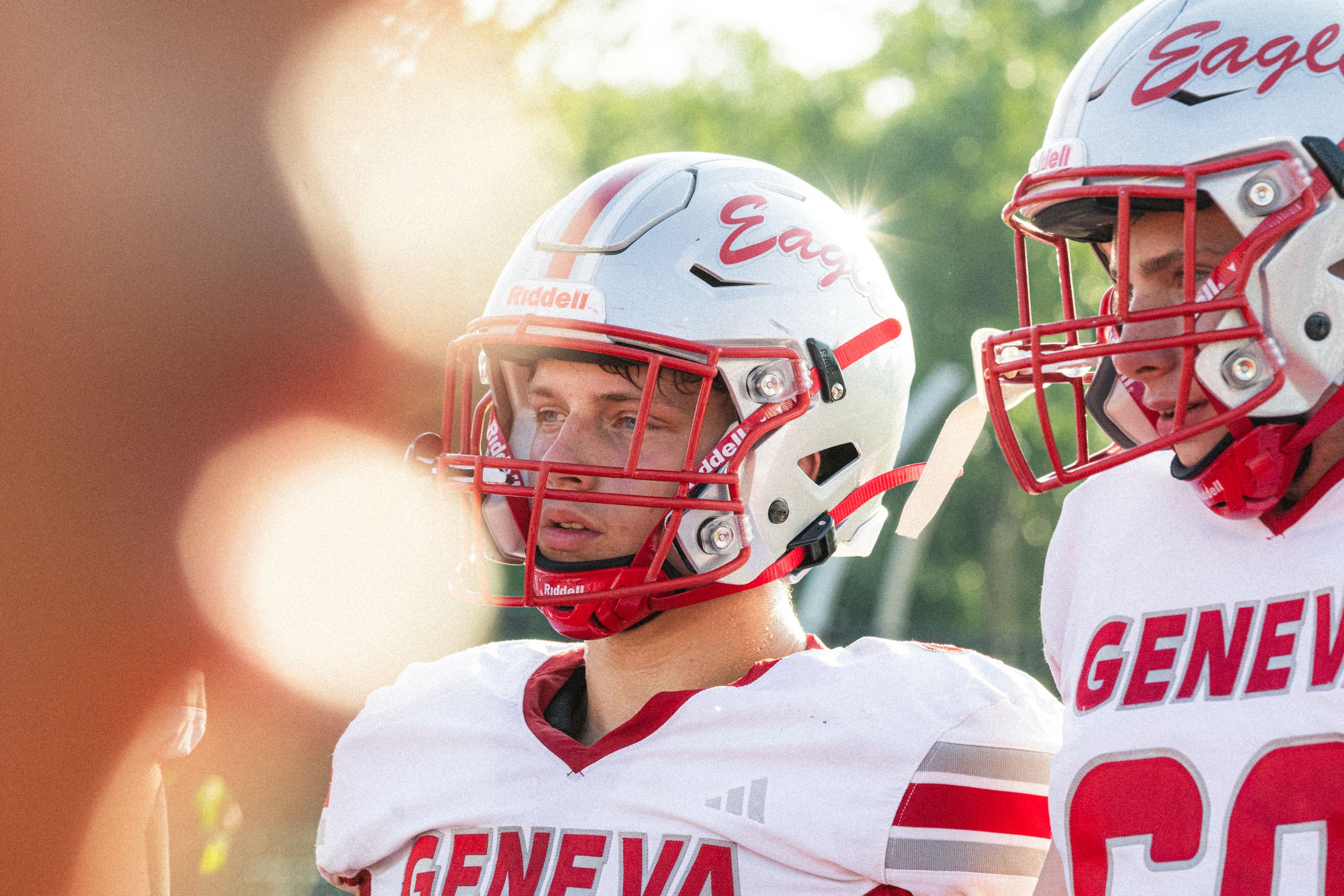Two Geneva Eagles football players in red and white helmets and uniforms stand on the sideline during a game.