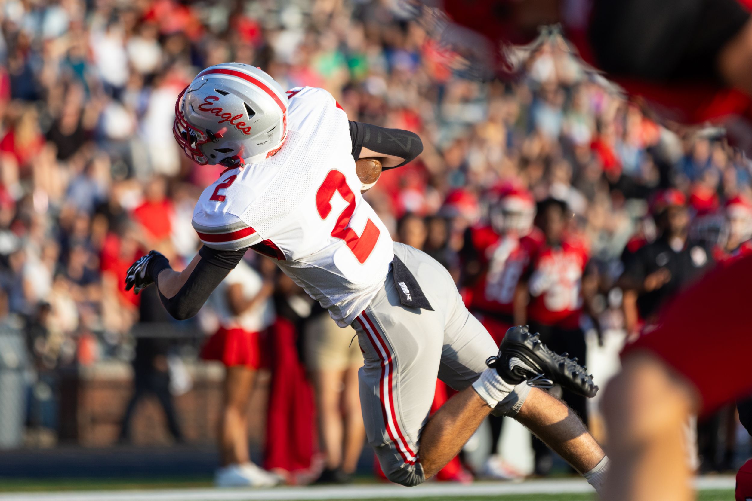 Geneva Eagles football player #2 leaping in the air during a game with fans in the stadium background.