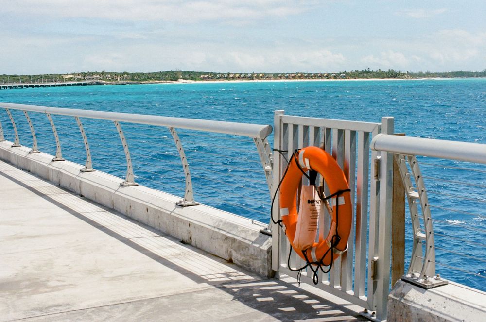 Orange life preserver ring mounted on a white metal railing of a pier overlooking calm blue tropical ocean waters.