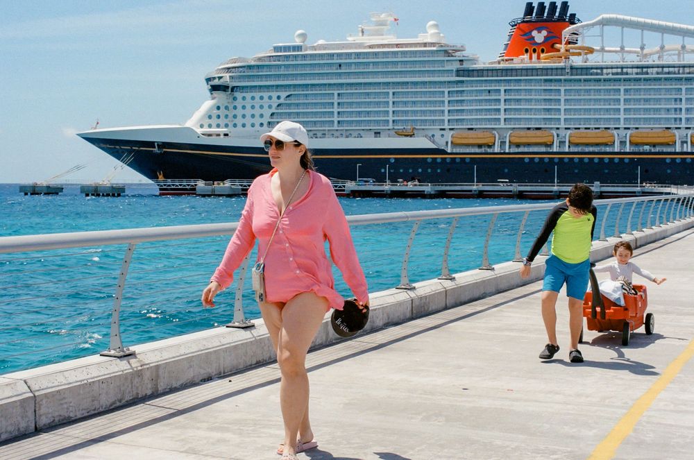 Woman in pink top walks on cruise ship dock with Disney cruise liner in background on sunny day.