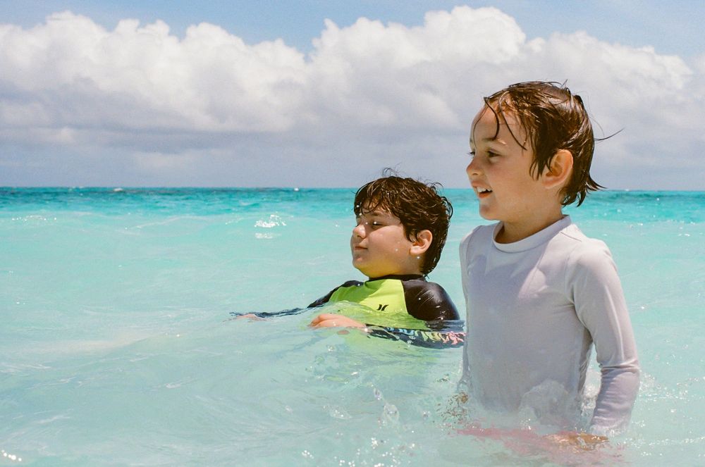 Two young boys playing in clear turquoise ocean water on a sunny beach day.