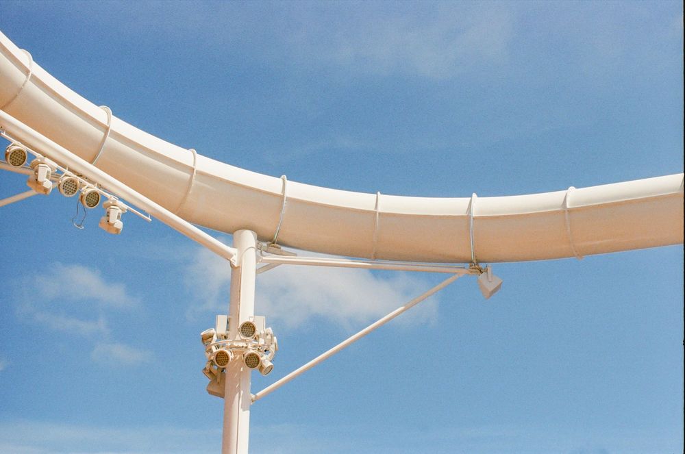 White roller coaster track curving against a bright blue sky with support structures and safety equipment visible.