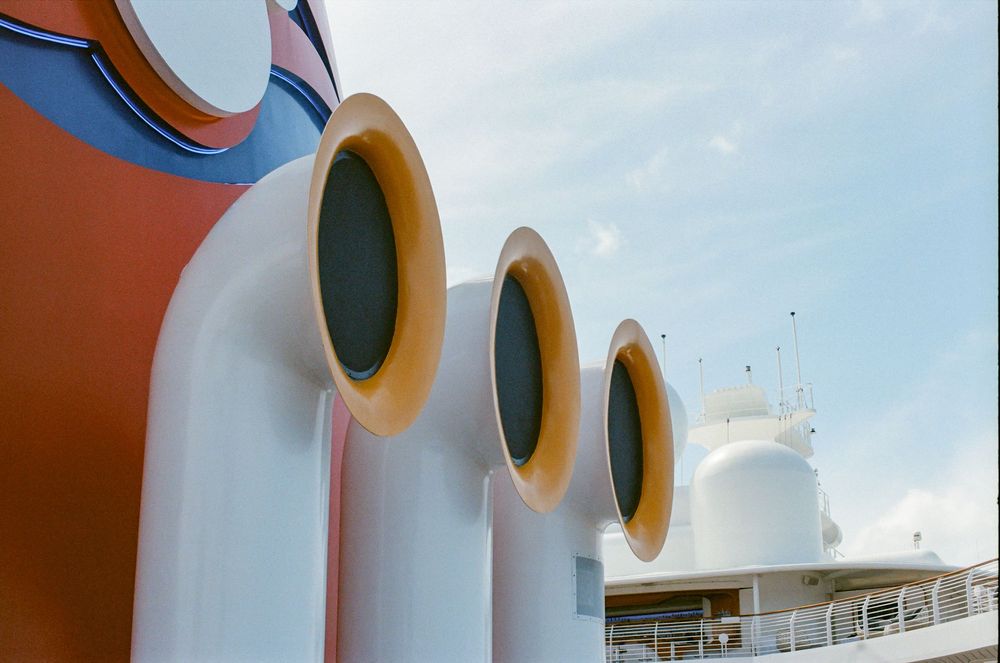 Close-up of colorful Disney cruise ship funnels with circular portholes against a blue sky.
