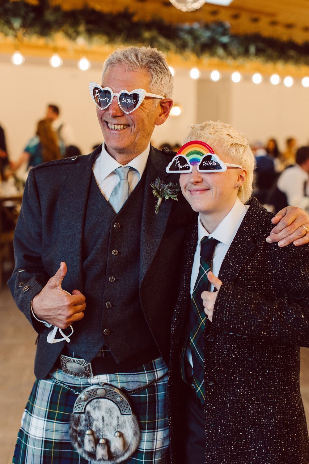 Two people in formal attire share a joyful moment at a wedding reception, with one wearing a traditional Scottish kilt.
