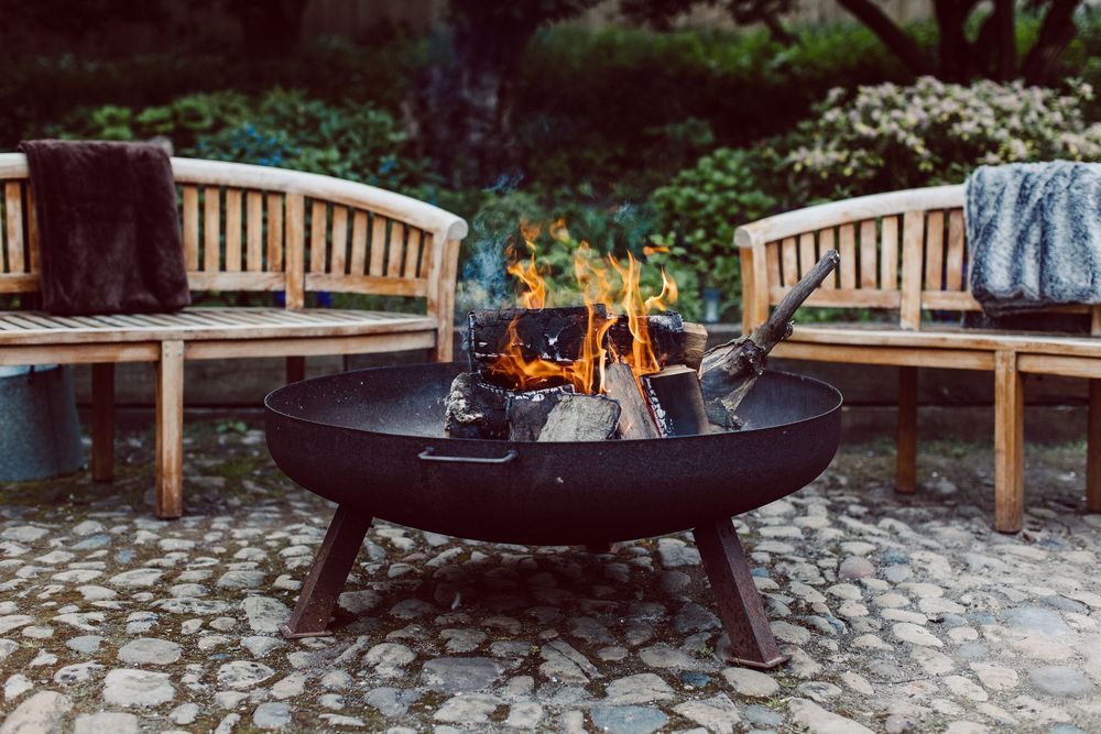 A series of cozy outdoor fire pits with wooden benches arranged in a row along a stone patio.