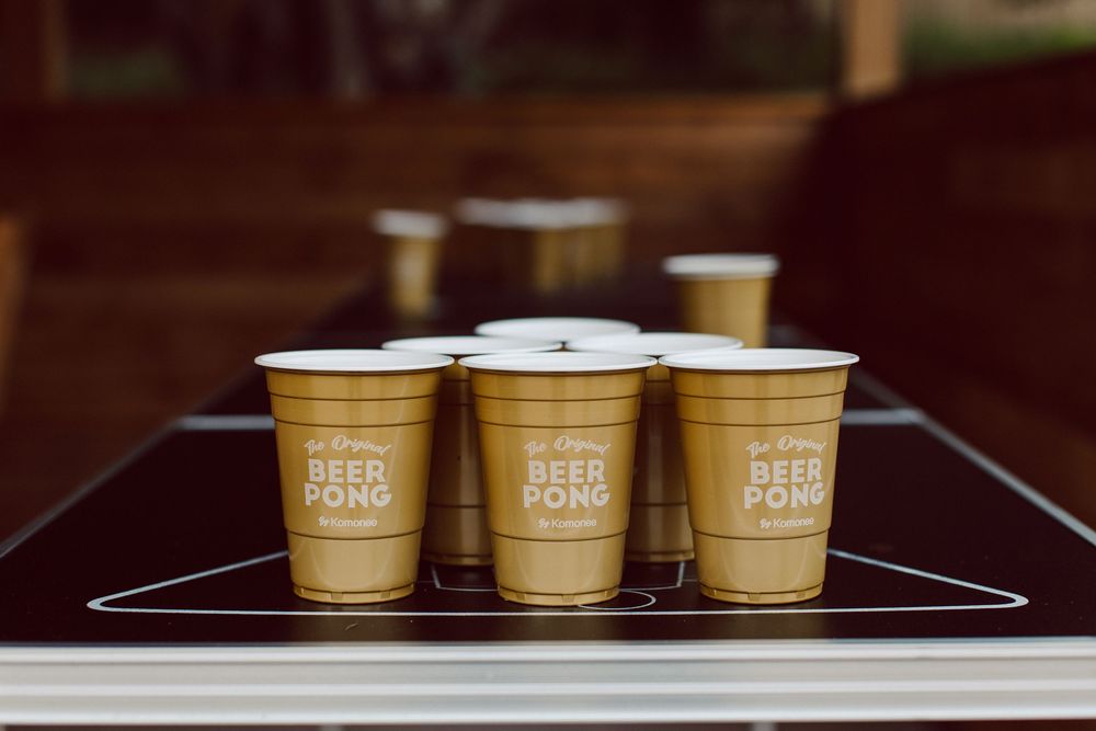 Gold paper coffee cups lined up on a wooden surface at a catering event.