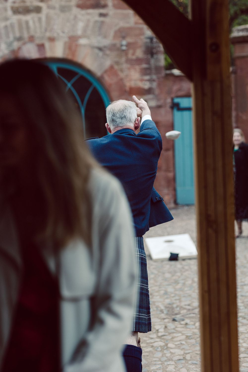 A person wearing a blue coat stands in a cobblestone courtyard near brick walls and wooden posts.